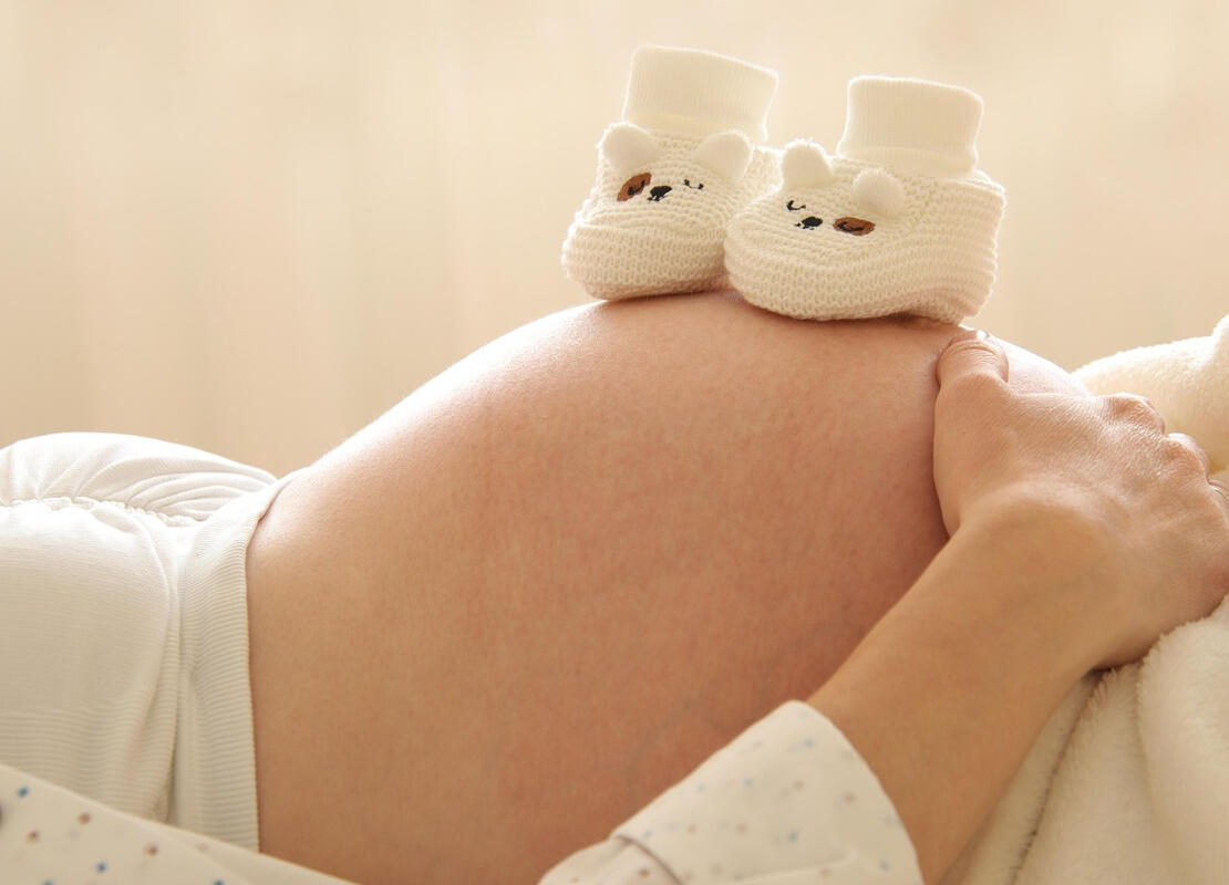 צילום של בטן הריון עם נעלי תינוק סרוגות עליה, כחלק מחבילת הכנה וליווי התפתחותי לקראת הלידה במעלה אדומים וירושלים. הדרכת הורים לעתיד עם טל יצחקי.